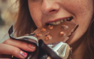 Woman eating chocolate bar (via Unsplash)